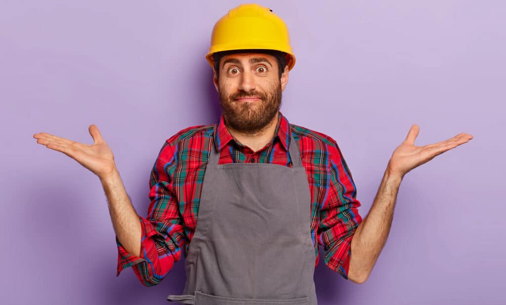 Man in a yellow hard hat and gray apron shrugs with arms outstretched against a purple background, conveying confusion or uncertainty.