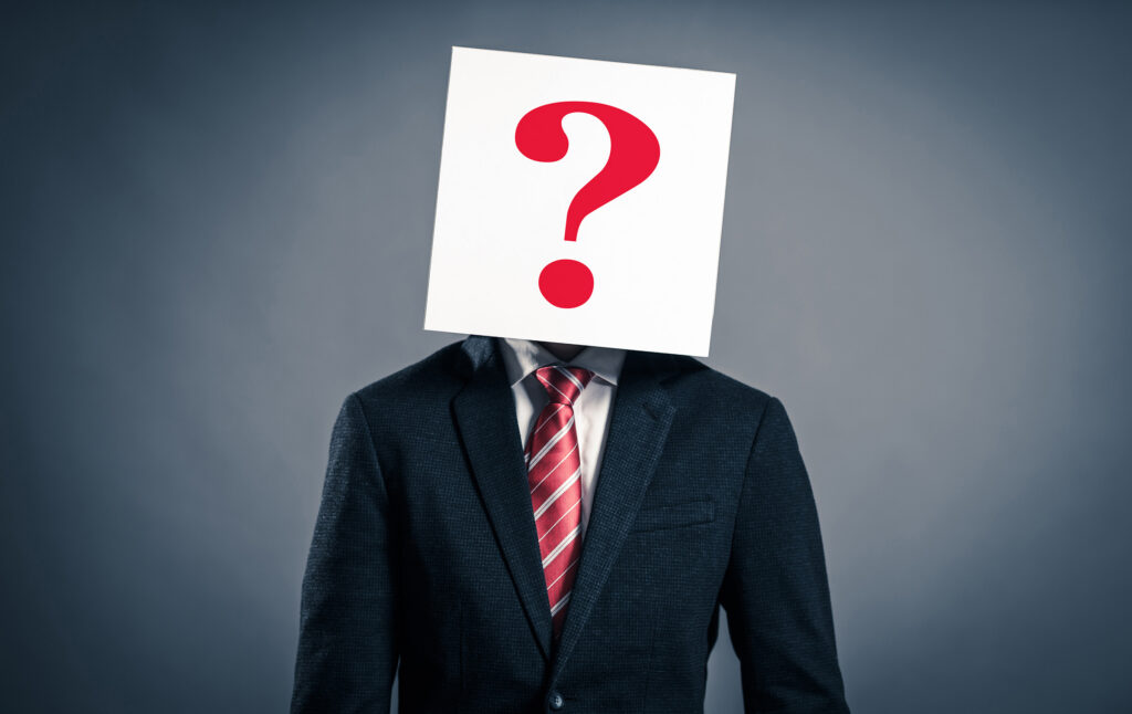Person in a dark suit and red striped tie with a white card covering their face, featuring a large red question mark in the center.